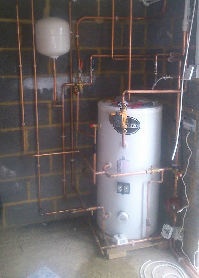 A white unvented hot water cylinder with new copper pipework against a block wall
