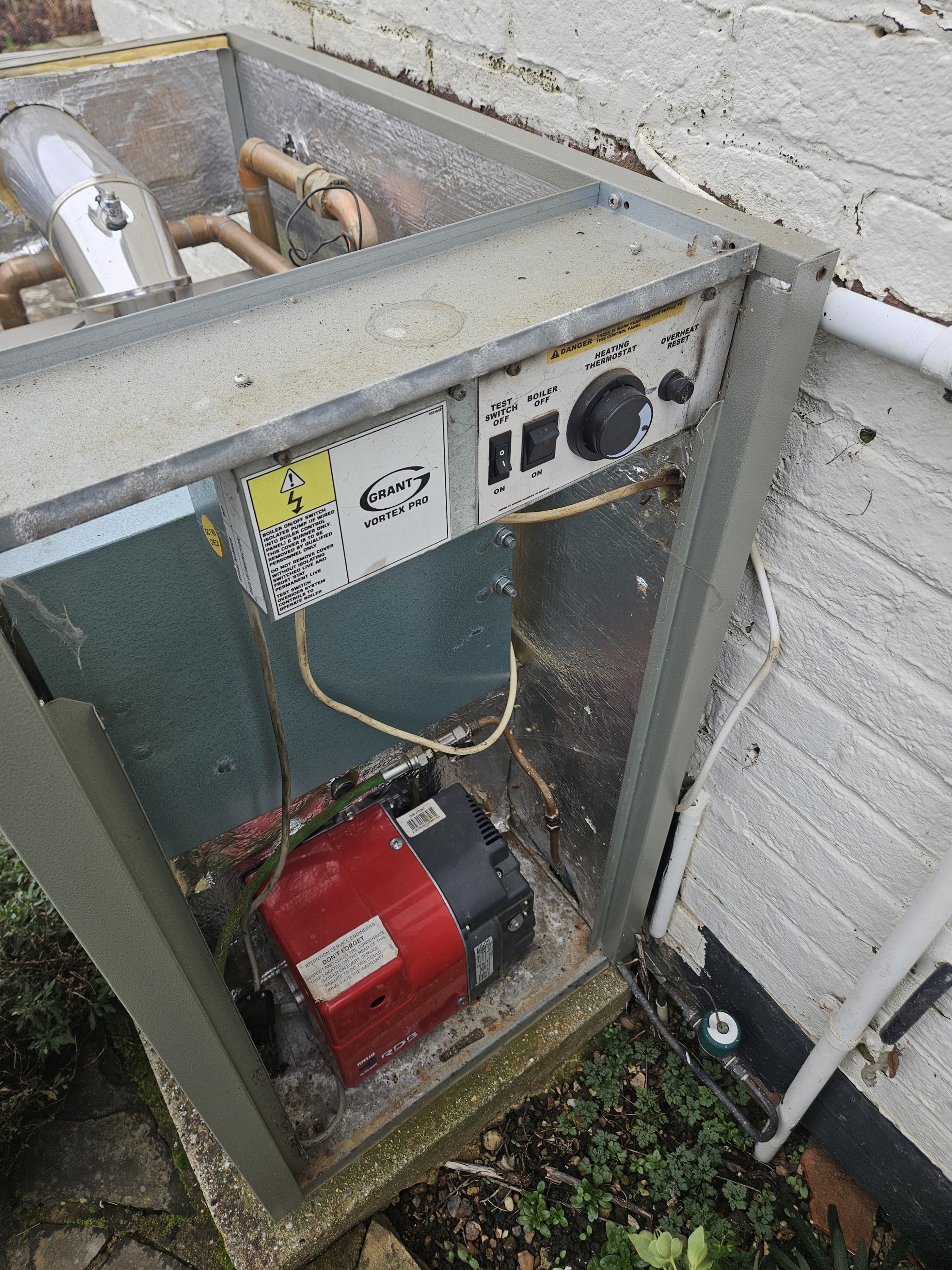 An outdoor Grant oil boiler with its casing open and the red burner showing