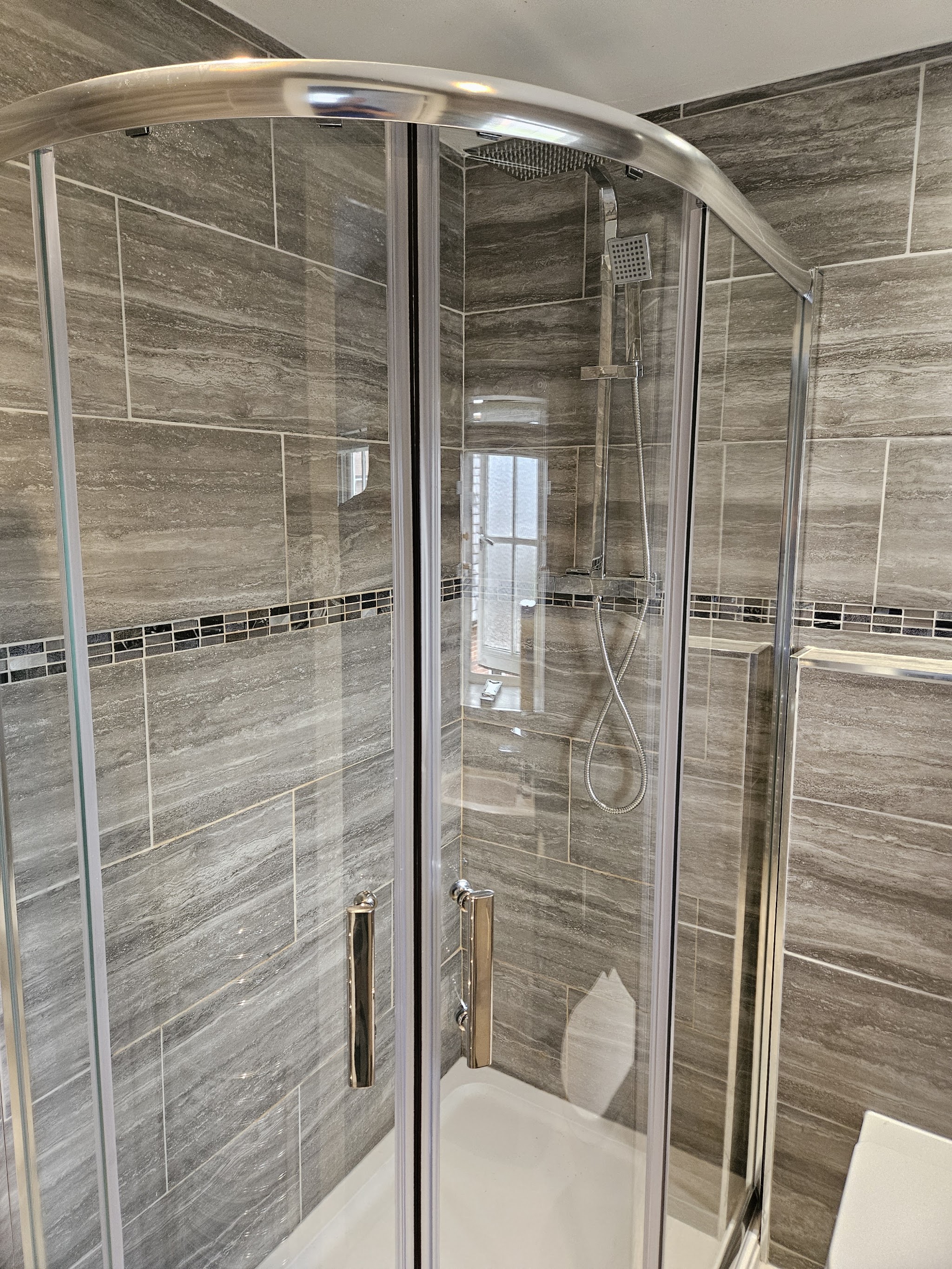 A finished quadrant shower enclosure with grey wood-effect tiles and a mosaic strip