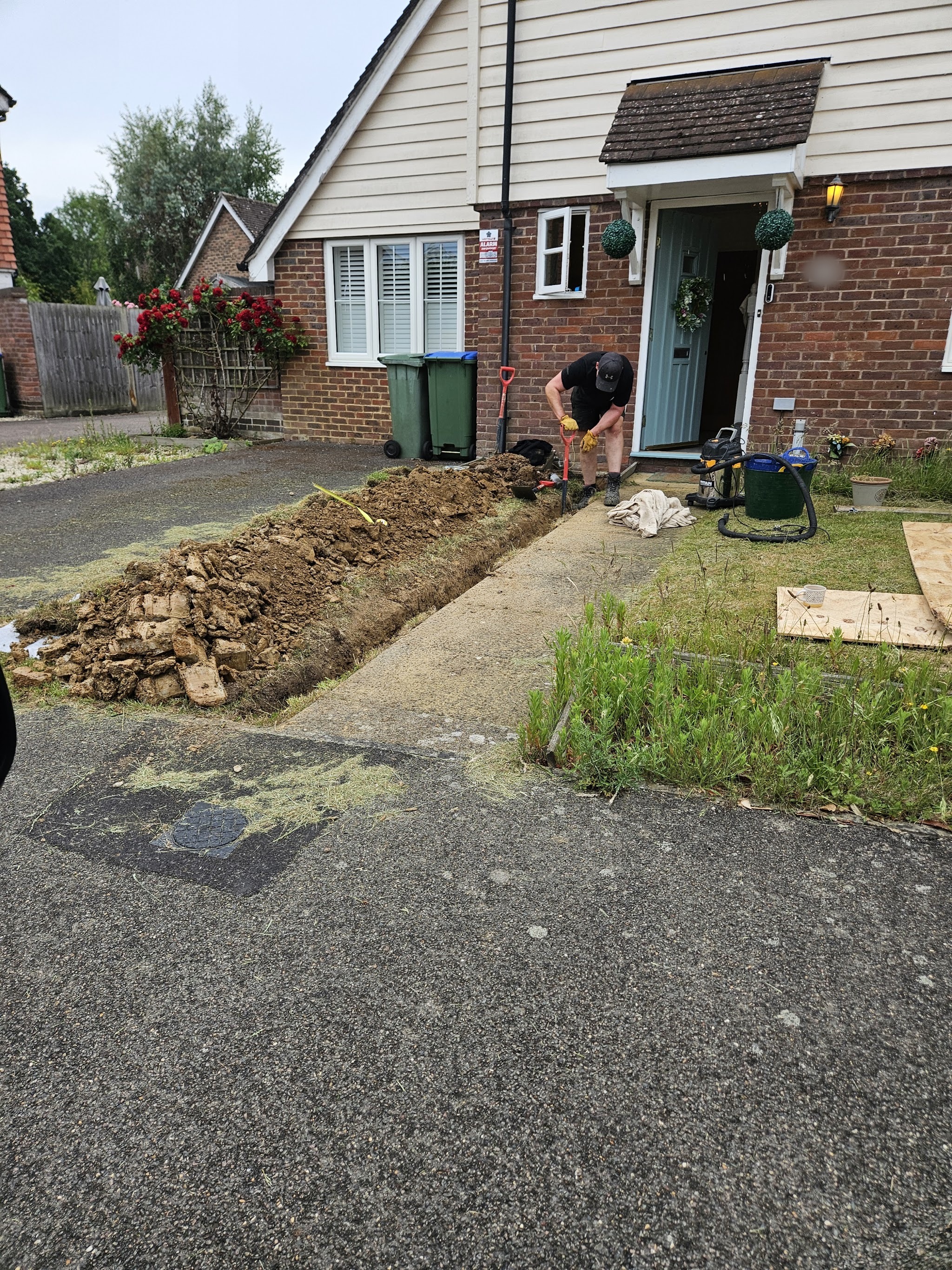 A trench dug along a front path up to a house, with a worker in the trench by the front door