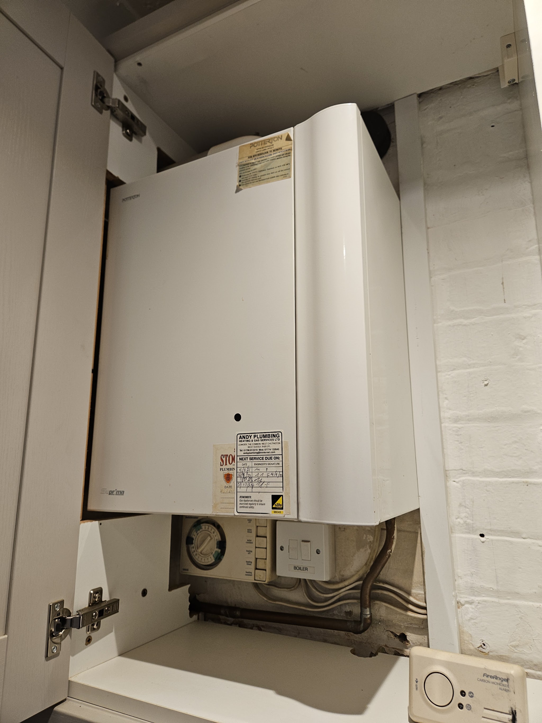 A wall-hung boiler in a kitchen cupboard with its programmer below