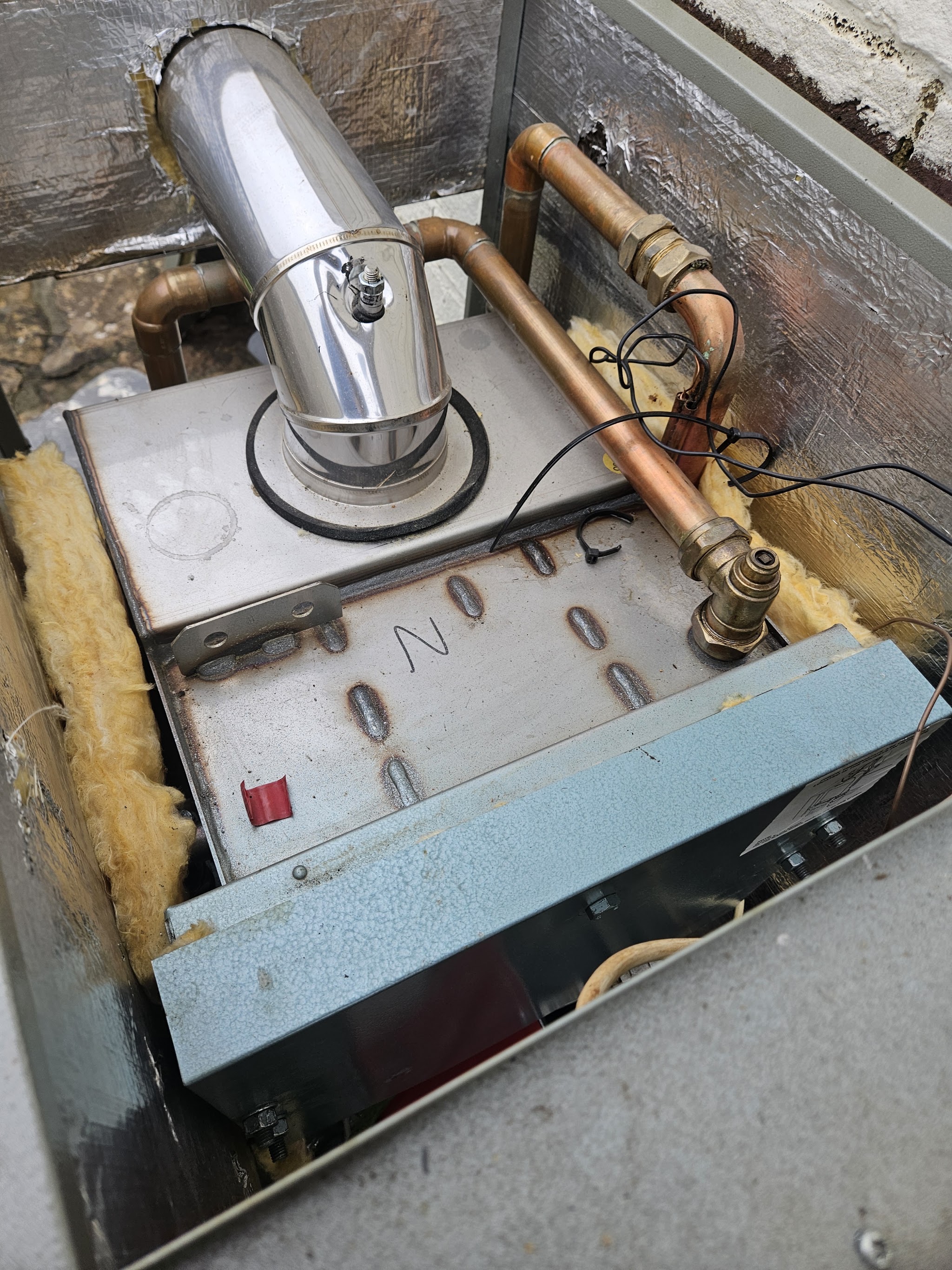 Inside an oil boiler with the cover removed, flue and copper connections visible