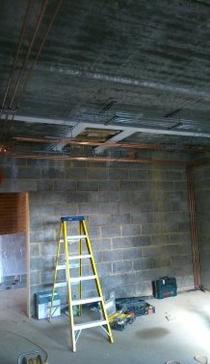 A large room mid-refurbishment with block walls, a ladder and pipework at the ceiling