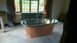 A copper roll-top bath beside a period window with a column radiator
