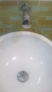 A vessel basin with a wall-mounted spout and green tiles